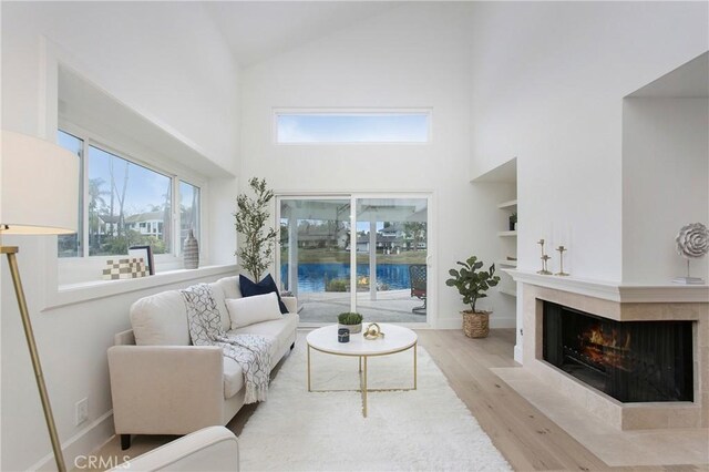 living area with high vaulted ceiling, wood finished floors, a fireplace with flush hearth, built in features, and baseboards