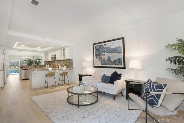 living room with a tray ceiling, a chandelier, and light hardwood / wood-style flooring