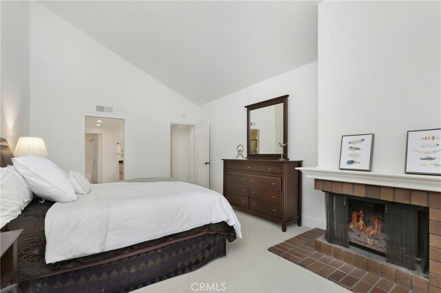 bedroom with ensuite bathroom, carpet floors, a tiled fireplace, and high vaulted ceiling