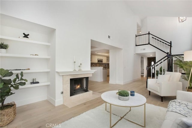 living room featuring built in shelves, a towering ceiling, a tiled fireplace, and light hardwood / wood-style flooring