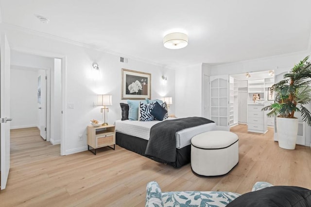 bedroom featuring ornamental molding, a spacious closet, and light wood-type flooring