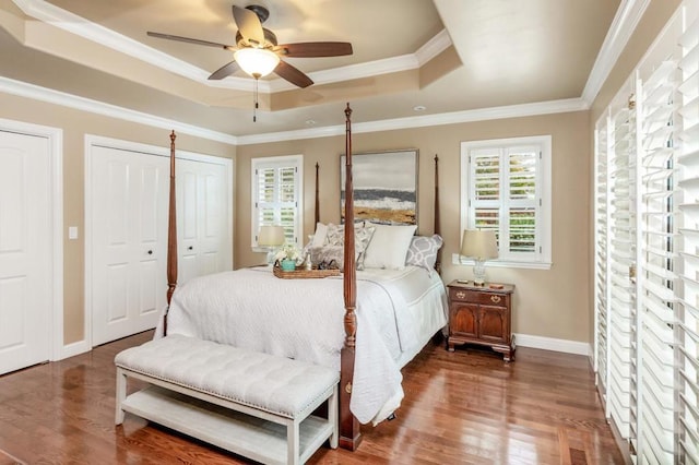 bedroom featuring a raised ceiling, crown molding, multiple closets, and dark hardwood / wood-style flooring