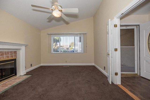 unfurnished living room with ceiling fan, lofted ceiling, a tiled fireplace, and dark carpet