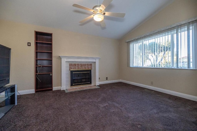 unfurnished living room with a tile fireplace, vaulted ceiling, ceiling fan, and dark carpet