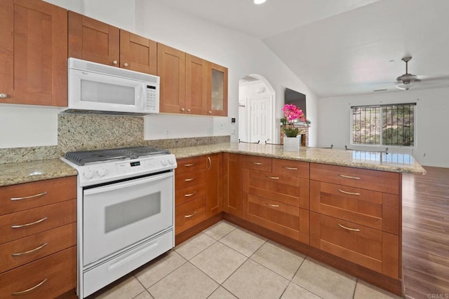 kitchen with white appliances, vaulted ceiling, kitchen peninsula, ceiling fan, and light stone countertops