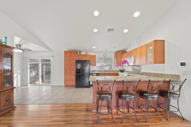 kitchen featuring plenty of natural light, a breakfast bar area, kitchen peninsula, and black refrigerator with ice dispenser