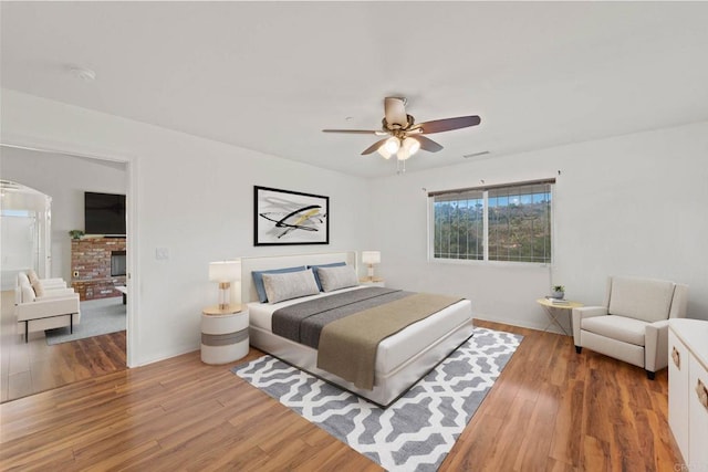 bedroom featuring ceiling fan, hardwood / wood-style floors, and a brick fireplace