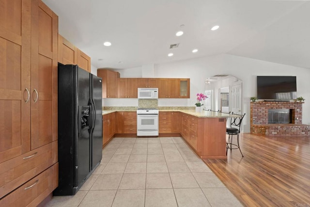 kitchen featuring a breakfast bar area, vaulted ceiling, a brick fireplace, kitchen peninsula, and white appliances