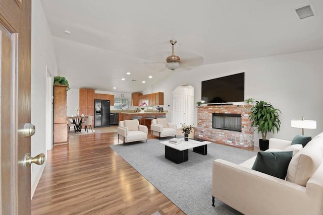 living room featuring vaulted ceiling, ceiling fan, light wood-type flooring, and a fireplace