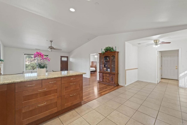 kitchen with light stone countertops, light tile patterned floors, lofted ceiling, and ceiling fan