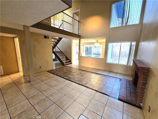 unfurnished living room featuring light tile patterned flooring, a towering ceiling, a textured ceiling, and ceiling fan