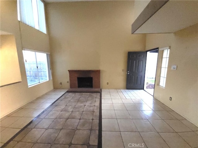 unfurnished living room featuring a high ceiling, a brick fireplace, and light tile patterned floors