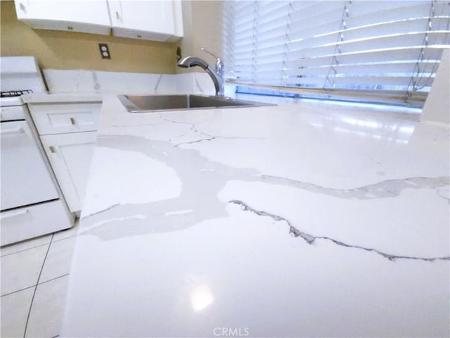 interior details with white cabinetry, white gas stove, sink, and light stone counters