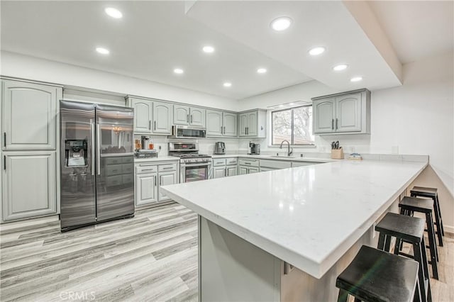 kitchen with sink, light hardwood / wood-style flooring, appliances with stainless steel finishes, a kitchen bar, and kitchen peninsula