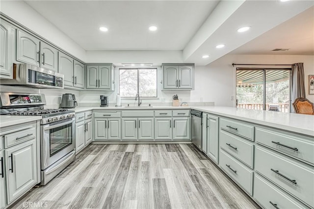 kitchen with sink, decorative backsplash, kitchen peninsula, stainless steel appliances, and light hardwood / wood-style flooring
