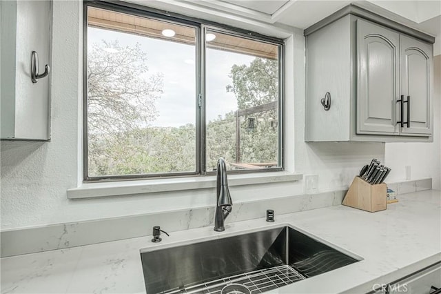 kitchen with light stone counters, plenty of natural light, gray cabinets, and sink
