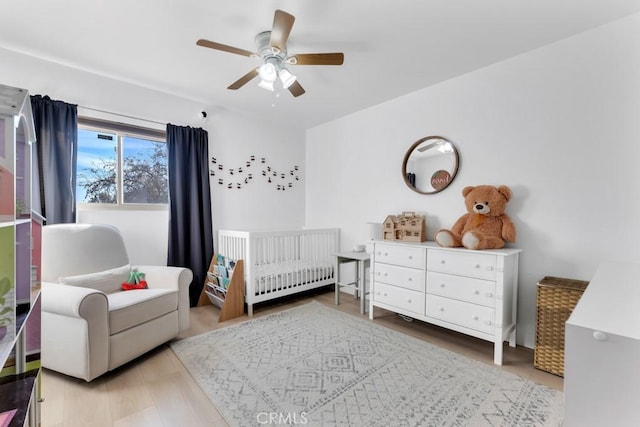 bedroom featuring radiator heating unit, wood-type flooring, a nursery area, and ceiling fan