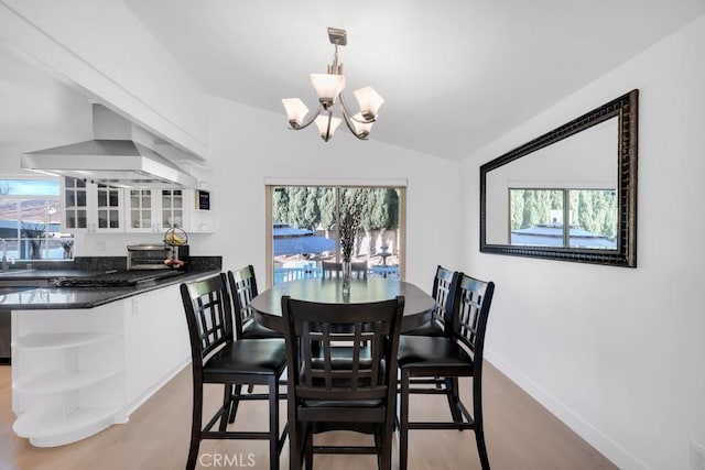 dining area featuring light wood-type flooring, sink, vaulted ceiling, and a notable chandelier