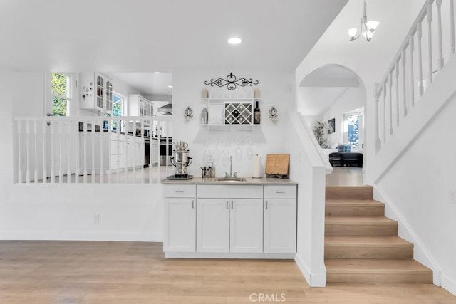 bar featuring white cabinetry, sink, hanging light fixtures, an inviting chandelier, and light hardwood / wood-style flooring