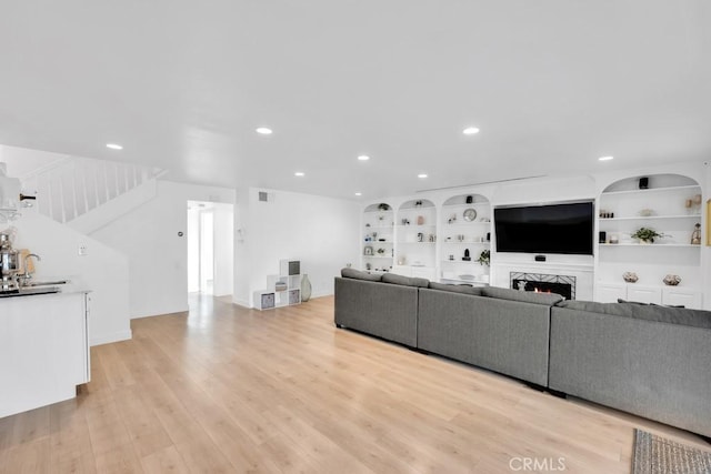 living room with built in shelves, sink, and light wood-type flooring