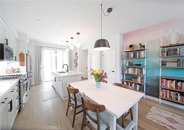 kitchen featuring white cabinetry, light hardwood / wood-style flooring, an island with sink, pendant lighting, and stainless steel appliances