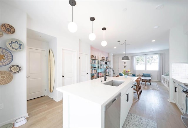 kitchen featuring sink, dishwasher, hanging light fixtures, white cabinets, and a center island with sink