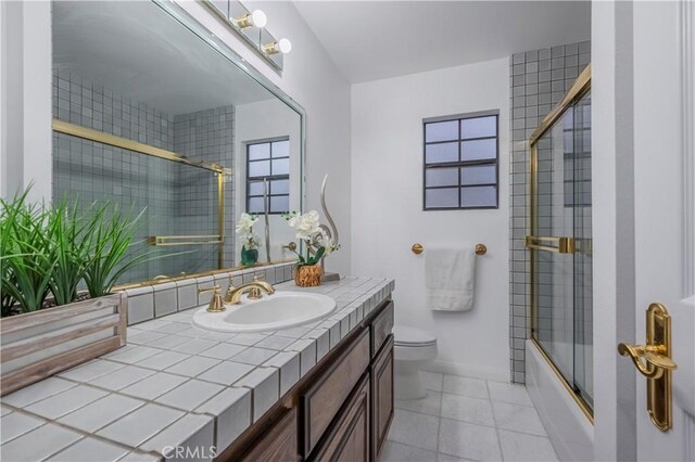 full bathroom with toilet, combined bath / shower with glass door, vanity, baseboards, and tile patterned floors