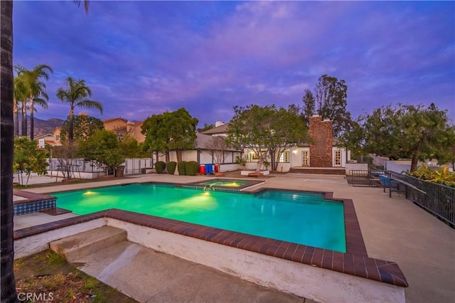 pool at dusk featuring an in ground hot tub and a patio area