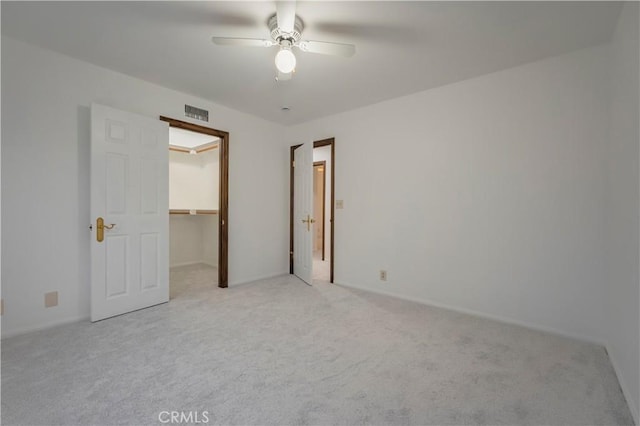 unfurnished bedroom featuring a walk in closet, light colored carpet, ceiling fan, and a closet