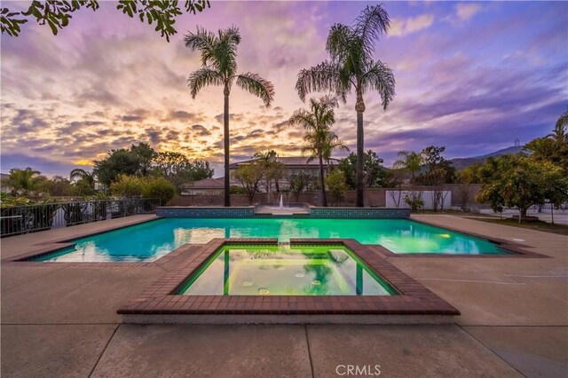 pool at dusk with an in ground hot tub and a patio area