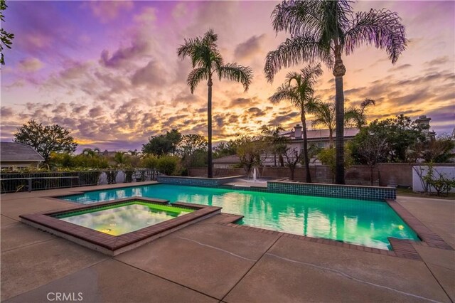 pool at dusk featuring a patio area and an in ground hot tub