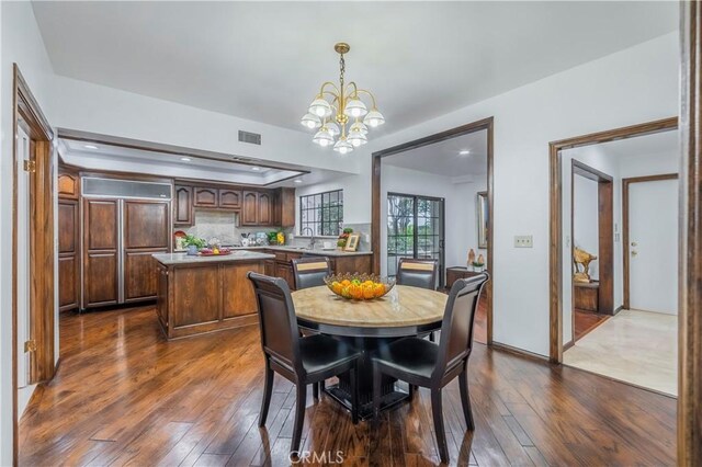 dining area featuring dark hardwood / wood-style flooring, sink, a tray ceiling, and an inviting chandelier