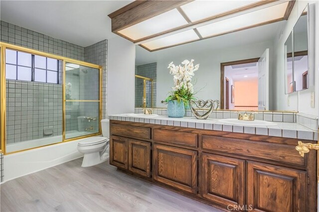 full bathroom featuring vanity, hardwood / wood-style floors, toilet, and combined bath / shower with glass door