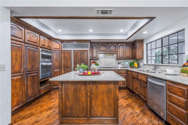 kitchen featuring appliances with stainless steel finishes, a center island, light stone counters, and a tray ceiling