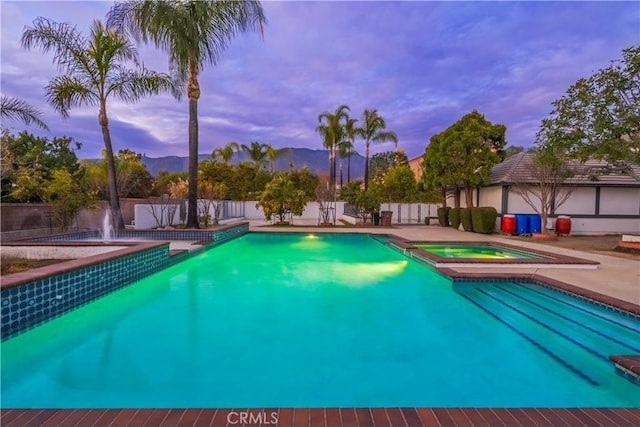 pool at dusk with an in ground hot tub