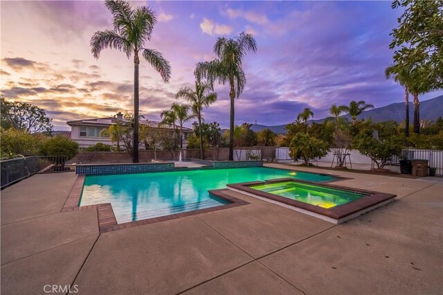 pool at dusk featuring a mountain view, a patio, and an in ground hot tub