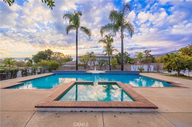 pool at dusk with a patio area and an in ground hot tub