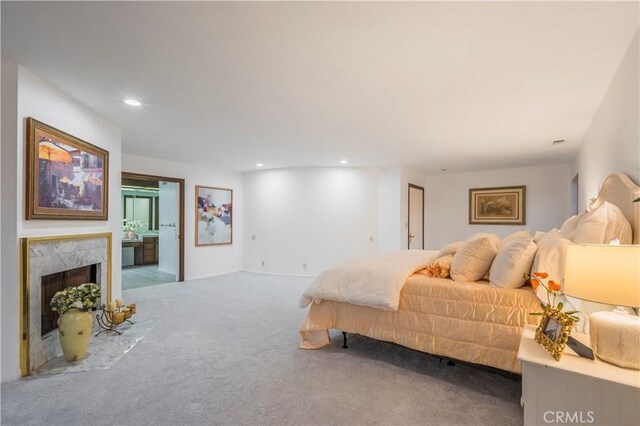 bedroom with carpet floors, connected bathroom, and a high end fireplace