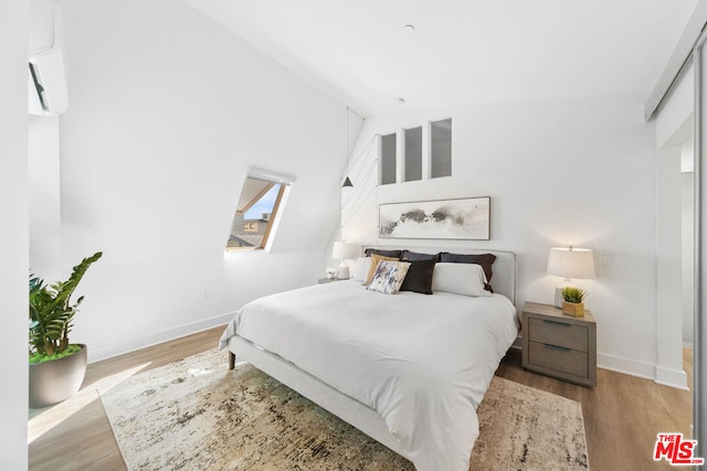 bedroom featuring an AC wall unit, high vaulted ceiling, and light hardwood / wood-style flooring