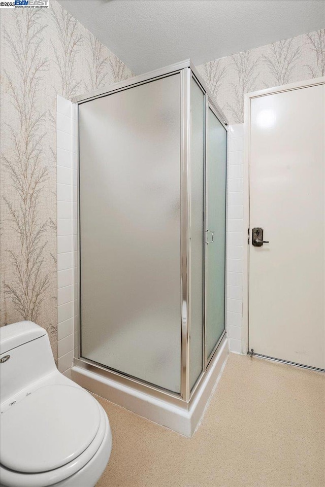 bathroom featuring toilet, a shower with door, and a textured ceiling