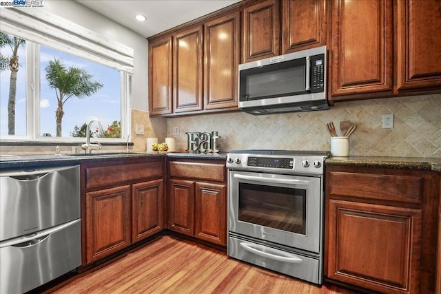 kitchen featuring dark stone countertops, sink, stainless steel appliances, and light hardwood / wood-style floors