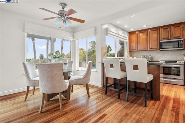 interior space featuring backsplash, a kitchen breakfast bar, ceiling fan, stainless steel appliances, and light hardwood / wood-style flooring