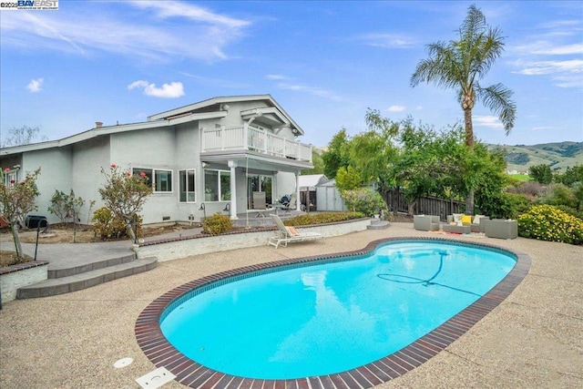 rear view of house featuring a shed, a balcony, a fenced in pool, and a patio area