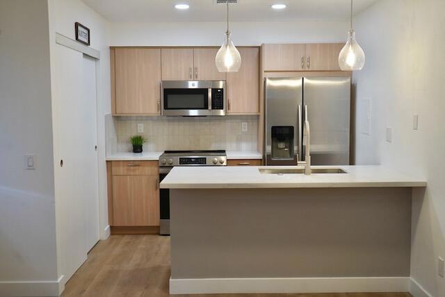 kitchen with decorative light fixtures, light brown cabinets, and appliances with stainless steel finishes