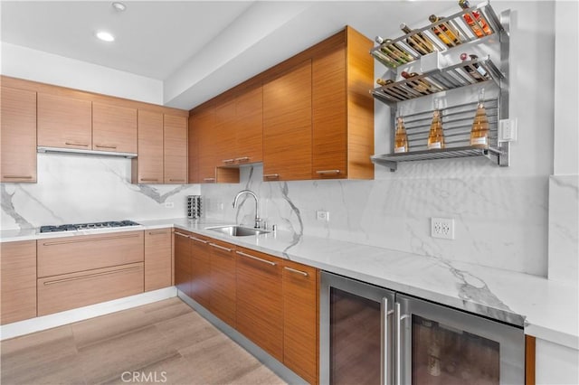 kitchen with stainless steel gas stovetop, sink, beverage cooler, decorative backsplash, and light hardwood / wood-style flooring