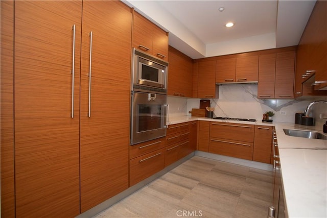 kitchen featuring a sink, brown cabinets, appliances with stainless steel finishes, light countertops, and under cabinet range hood