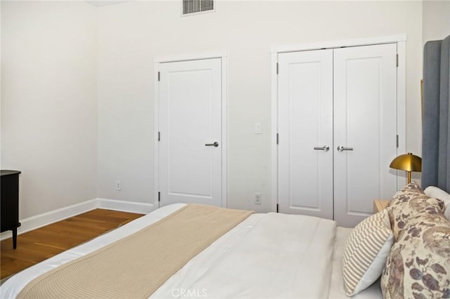 bedroom featuring baseboards, wood finished floors, visible vents, and a closet