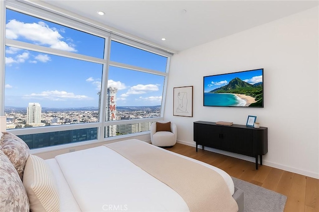 bedroom featuring a view of city, baseboards, wood finished floors, and recessed lighting