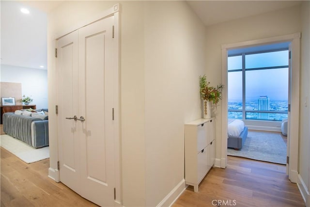 hall featuring baseboards, light wood finished floors, and recessed lighting