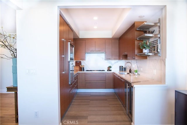 kitchen with a sink, decorative backsplash, brown cabinets, open shelves, and appliances with stainless steel finishes